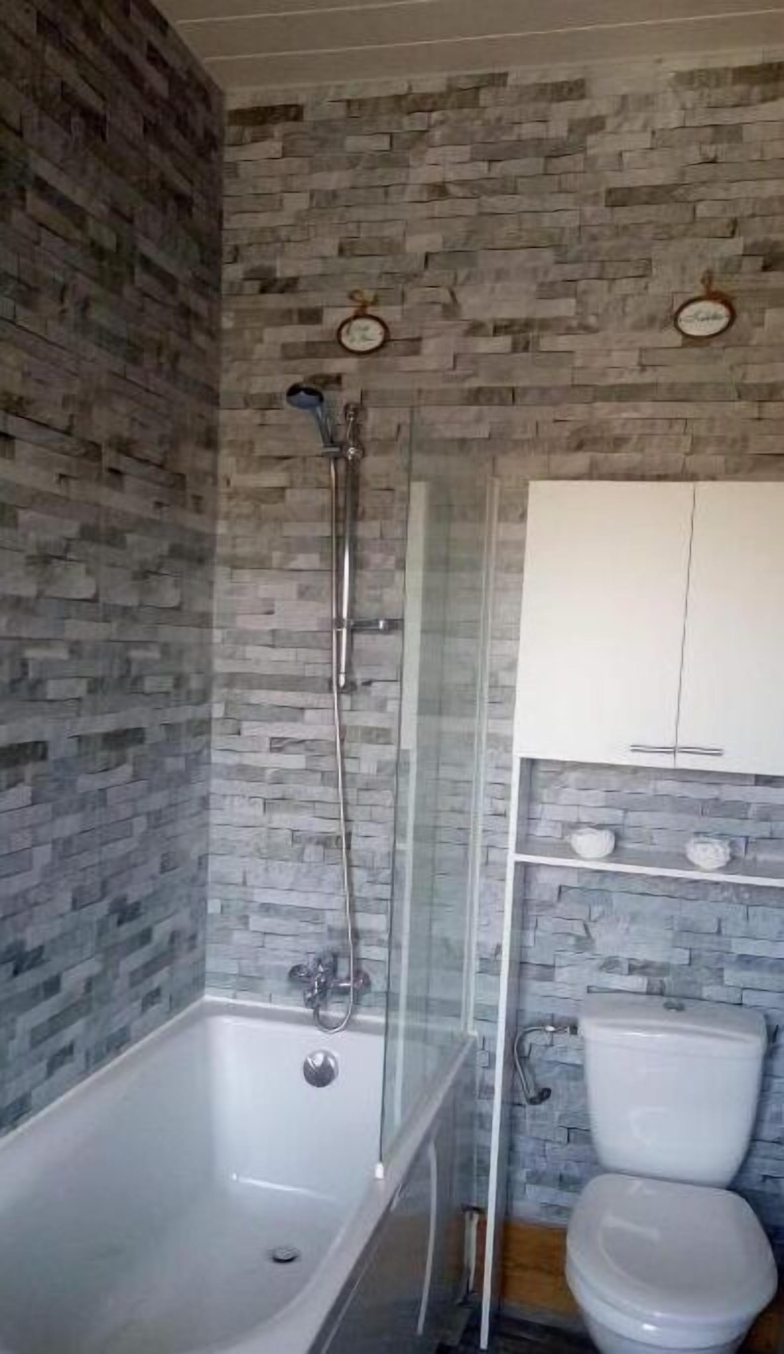 A bathroom with a stone wall, a bathtub, a shower, and a toilet.
