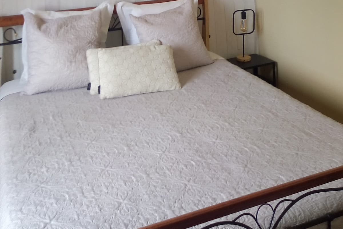 A bedroom with a bed, white bedding, a woven pendant light, and three beach-themed wall art pieces.
