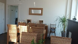 Un comedor con sillas de mimbre y una mesa, un espejo en la pared y una planta en maceta.
