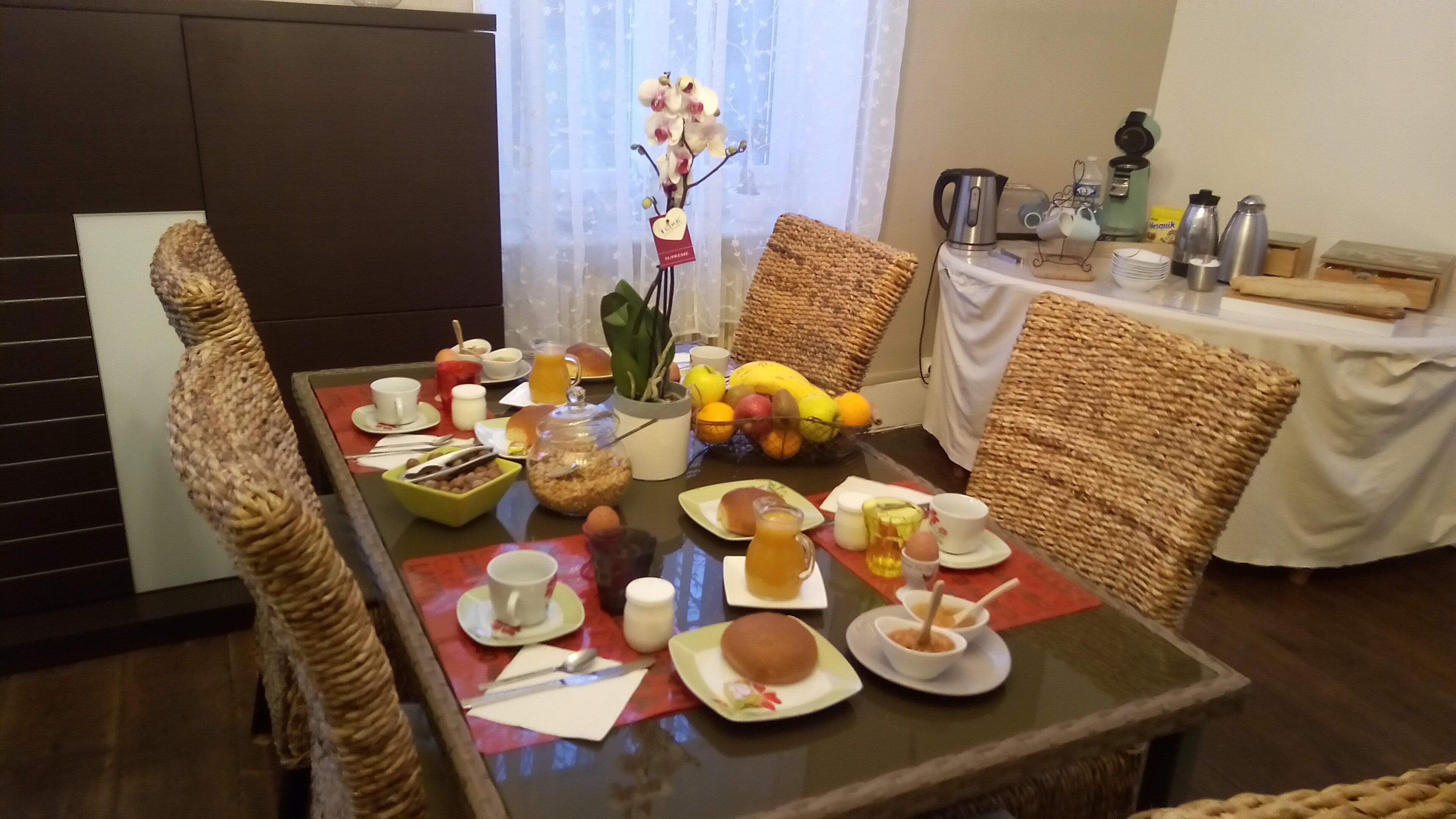 A dining table set with breakfast items, including fruits, bread, and beverages, surrounded by wicker chairs.