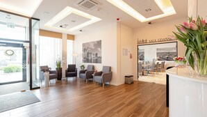 A modern hotel lobby with wooden flooring, grey armchairs, a reception desk, and a wall-mounted sign reading "SALA GDANSK." - Hotel Platan (Gdansk)