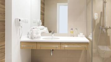 A modern bathroom with a glass-enclosed shower, a white sink with a mirror, and a hairdryer on the wall.