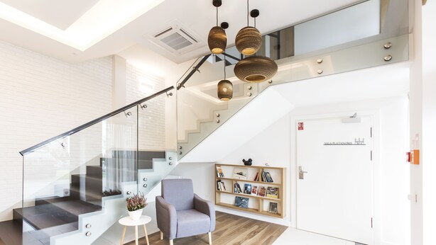 A modern living area with a staircase, a grey armchair, a small white table, and a bookshelf. - Hotel Platan (Gdansk)