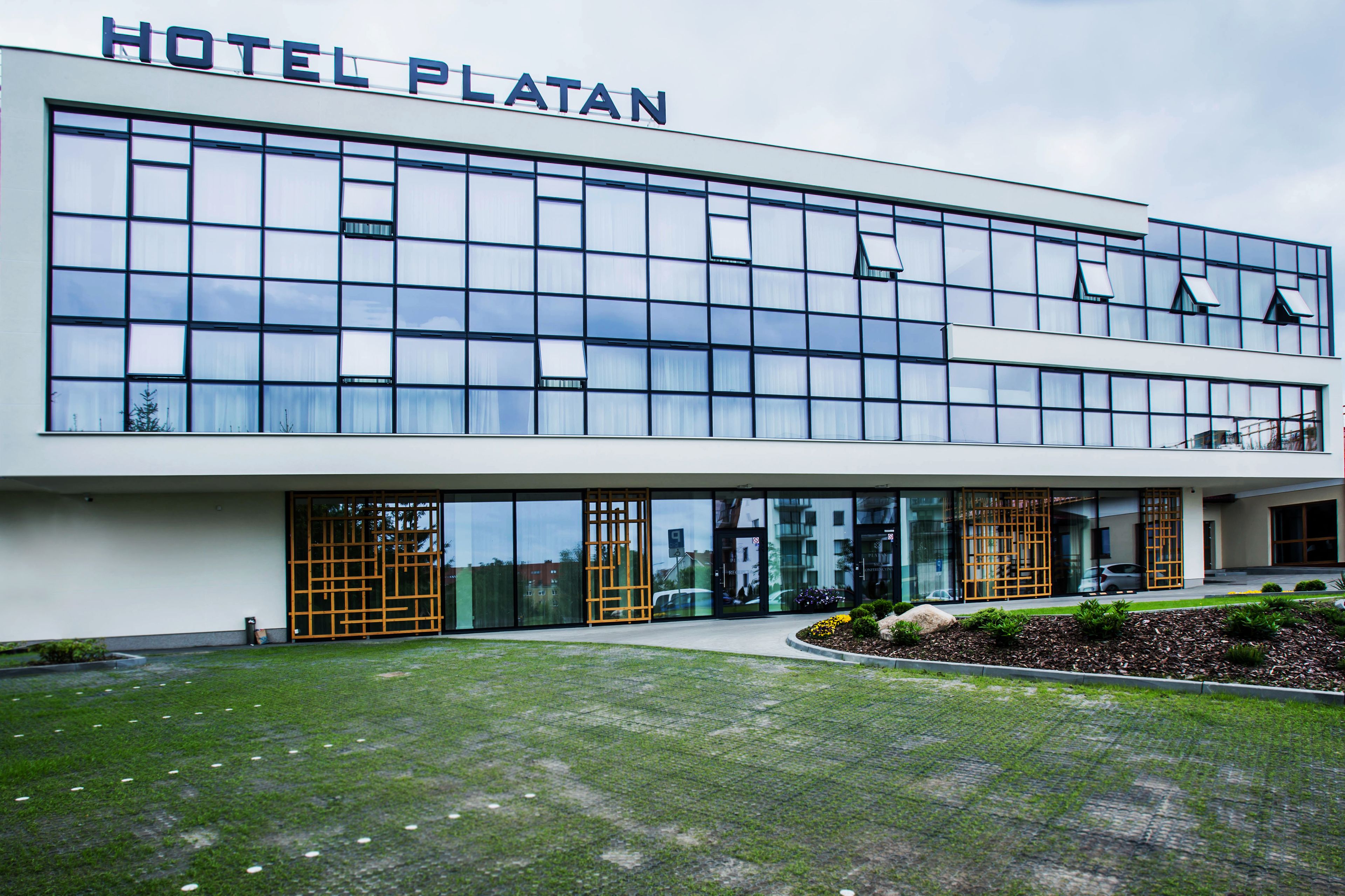 Moderni hotellirakennus, jossa on suuret lasi-ikkunat ja kyltti, jossa lukee ”HOTEL PLATAN”.
