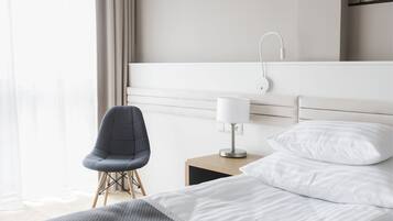 A hotel room with a bed, a chair, a nightstand with a lamp, and a view of the outdoors.