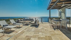 Un patio exterior con vistas al mar, amueblado con sillones de descanso y una mesa de comedor.