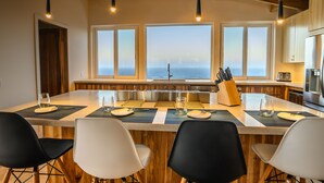 Una cocina con una isla grande, taburetes de bar y vista al océano.
