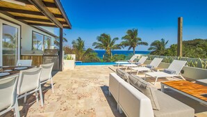 Un patio con piscina, sillas de descanso y una zona de cocina con parrilla.