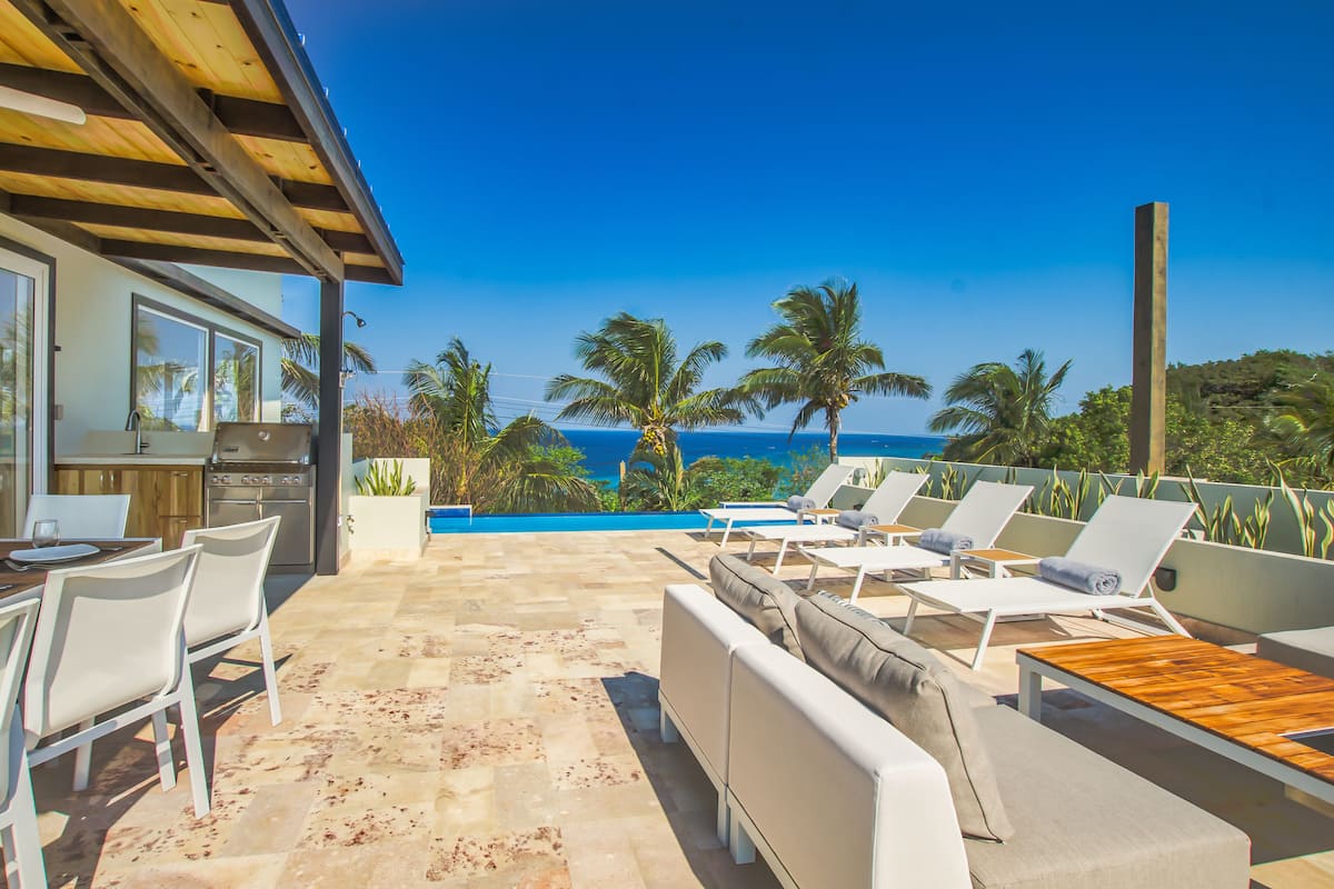 Un patio con piscina, sillas de descanso y una zona de cocina con parrilla.