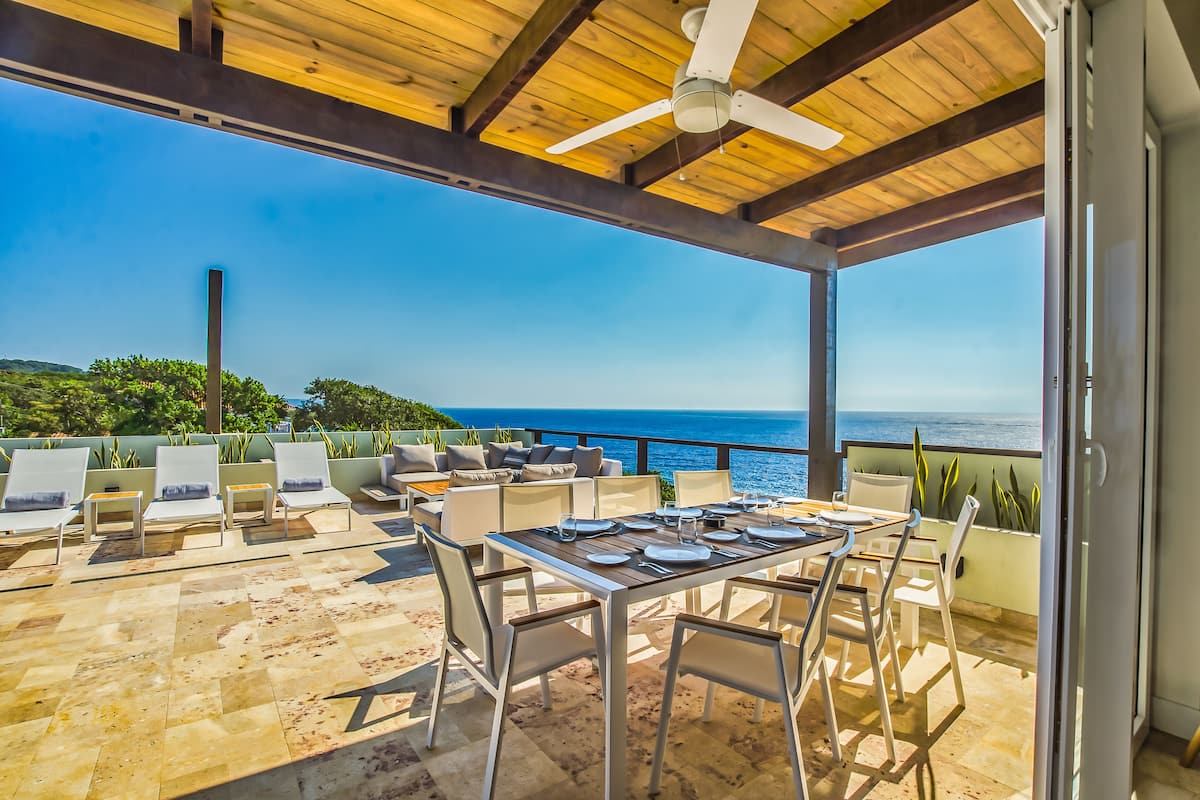 Un patio exterior con mesa lista para comer, sillas de descanso y vista al mar.