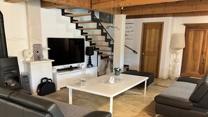 Uma sala de estar moderna com uma mesa branca, sofás de couro preto, uma TV de tela plana, lareira e uma escada.
