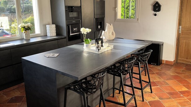 Uma cozinha moderna com uma ilha central, banquetas de bar e um relógio na parede.