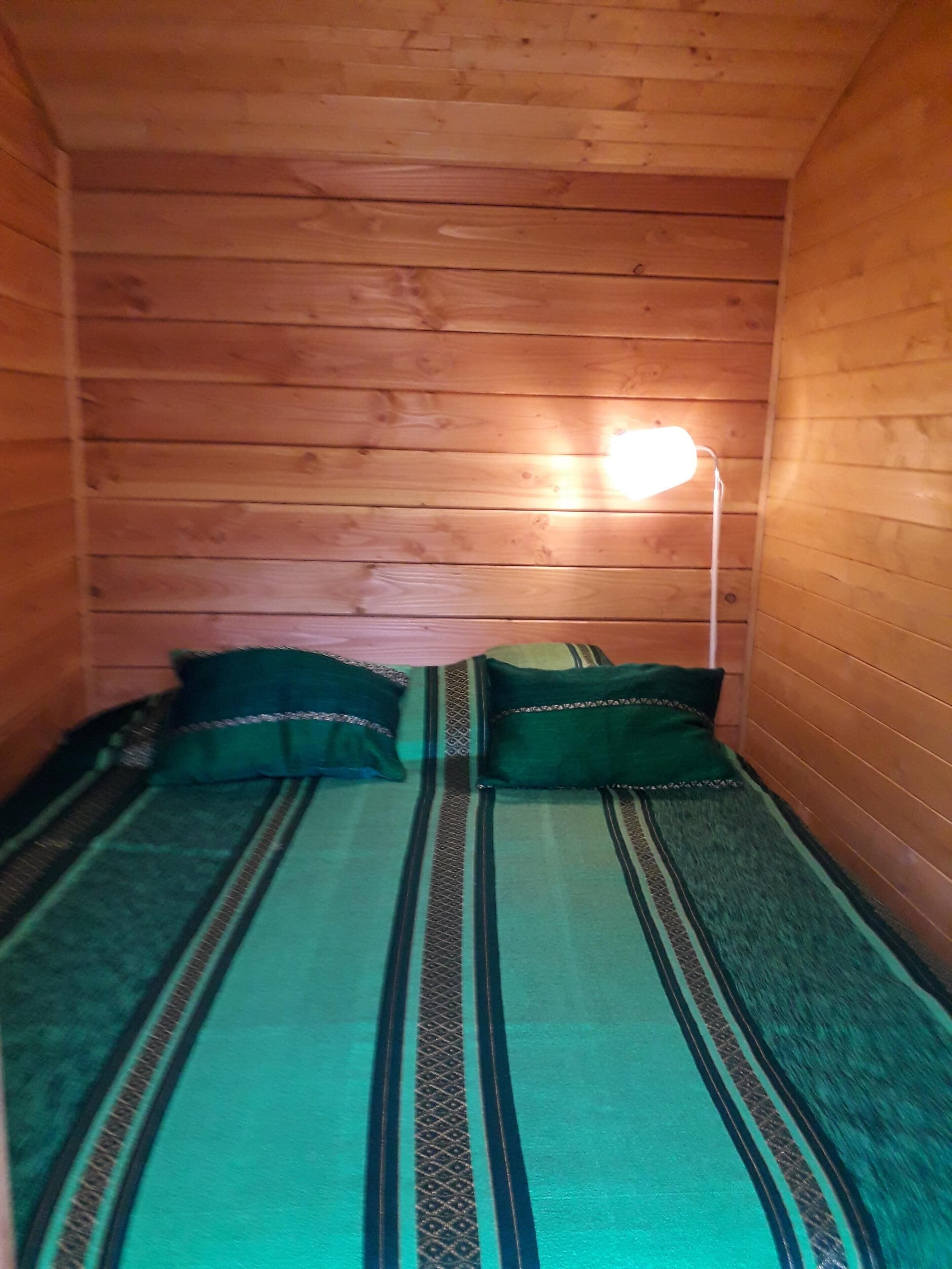 A small, cozy room with wooden walls and a single bed with green bedding.