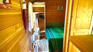 A small, wooden cabin room with a bed, a wardrobe, and a small table. - A wooden caravan at Domaine de la Morétie (CUBLAC)