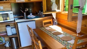 A compact kitchen with wooden cabinets, a microwave, a sink, and a dining area with a table and chairs. - A wooden caravan at Domaine de la Morétie (CUBLAC)