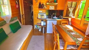 A cozy cabin with a wooden interior, a bed, a dining table, and a kitchenette. - A wooden caravan at Domaine de la Morétie (CUBLAC)