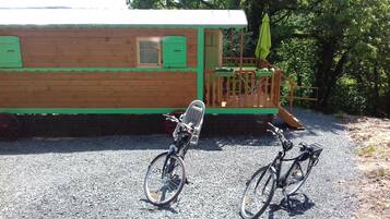 Una baita di legno con esterno verde, un piccolo portico e due biciclette parcheggiate davanti.