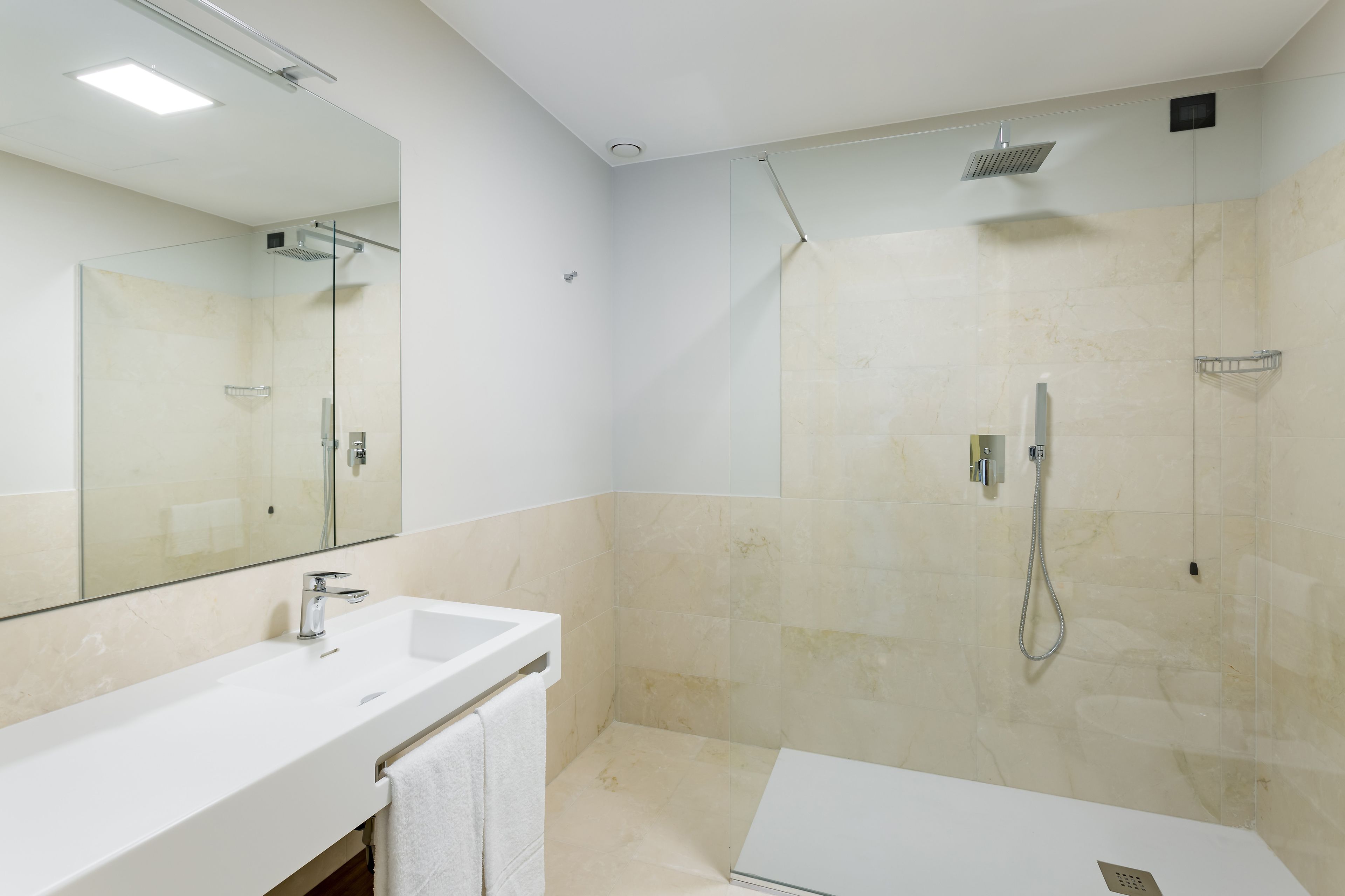 Een moderne badkamer met een grote spiegel, een witte wastafel, een douche en een toilet.