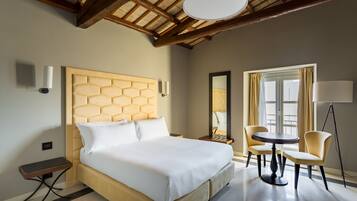 Ein Hotelzimmer mit einem großen Bett, einem runden Tisch, zwei Stühlen, einer Stehlampe und einem fensterbepflanzten Fenster.
