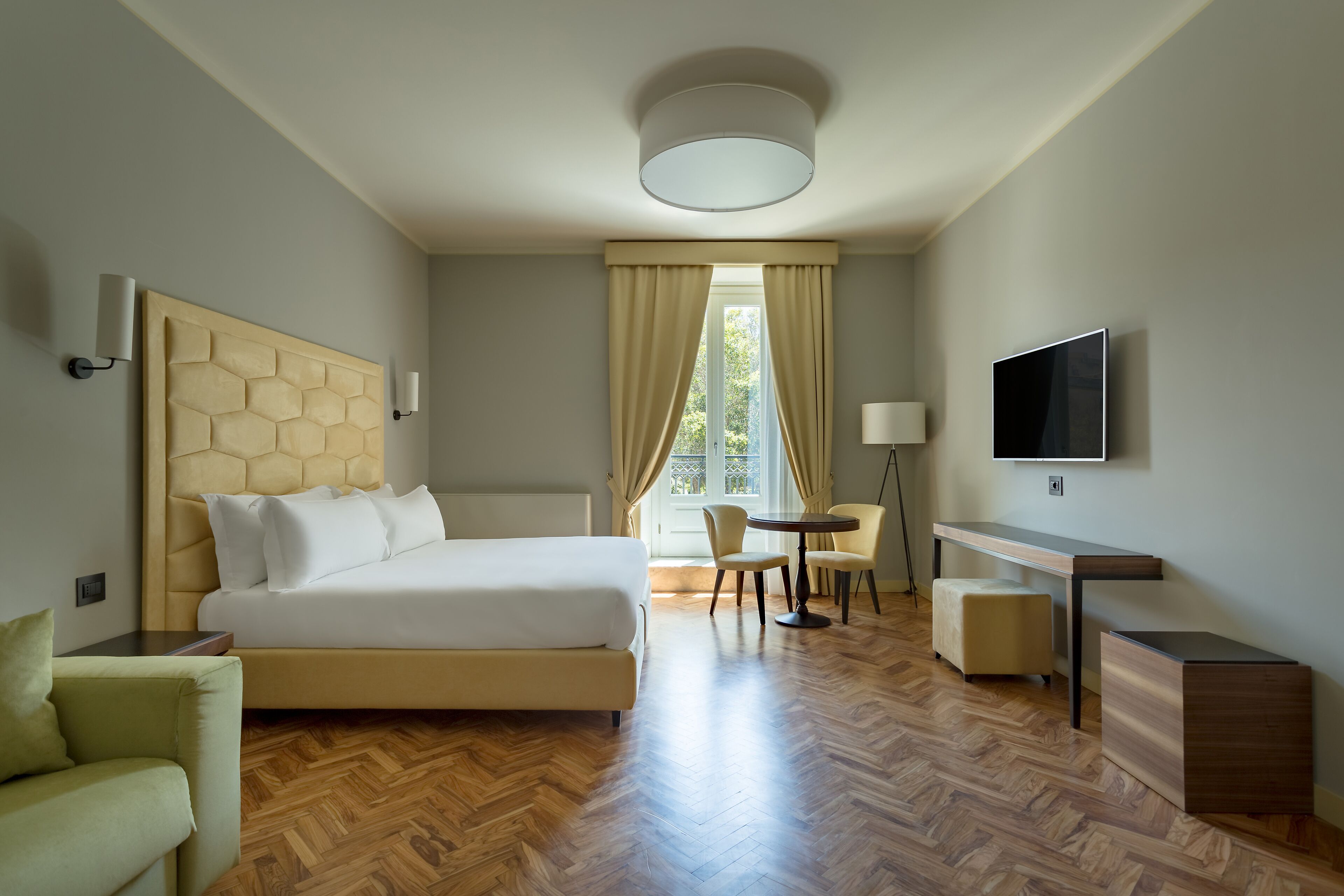 A hotel room with a large bed, a desk, a chair, a TV, and a window with curtains.