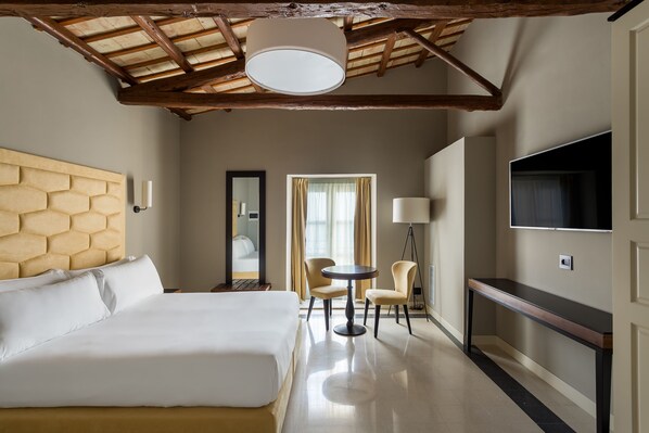 A hotel room with a large bed, a small round table, two chairs, a TV, and a mirror.
