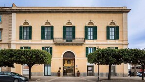 A historic building with a symmetrical facade, green shutters, and a central entrance with a balcony. - Room of Andrea (Trapani)