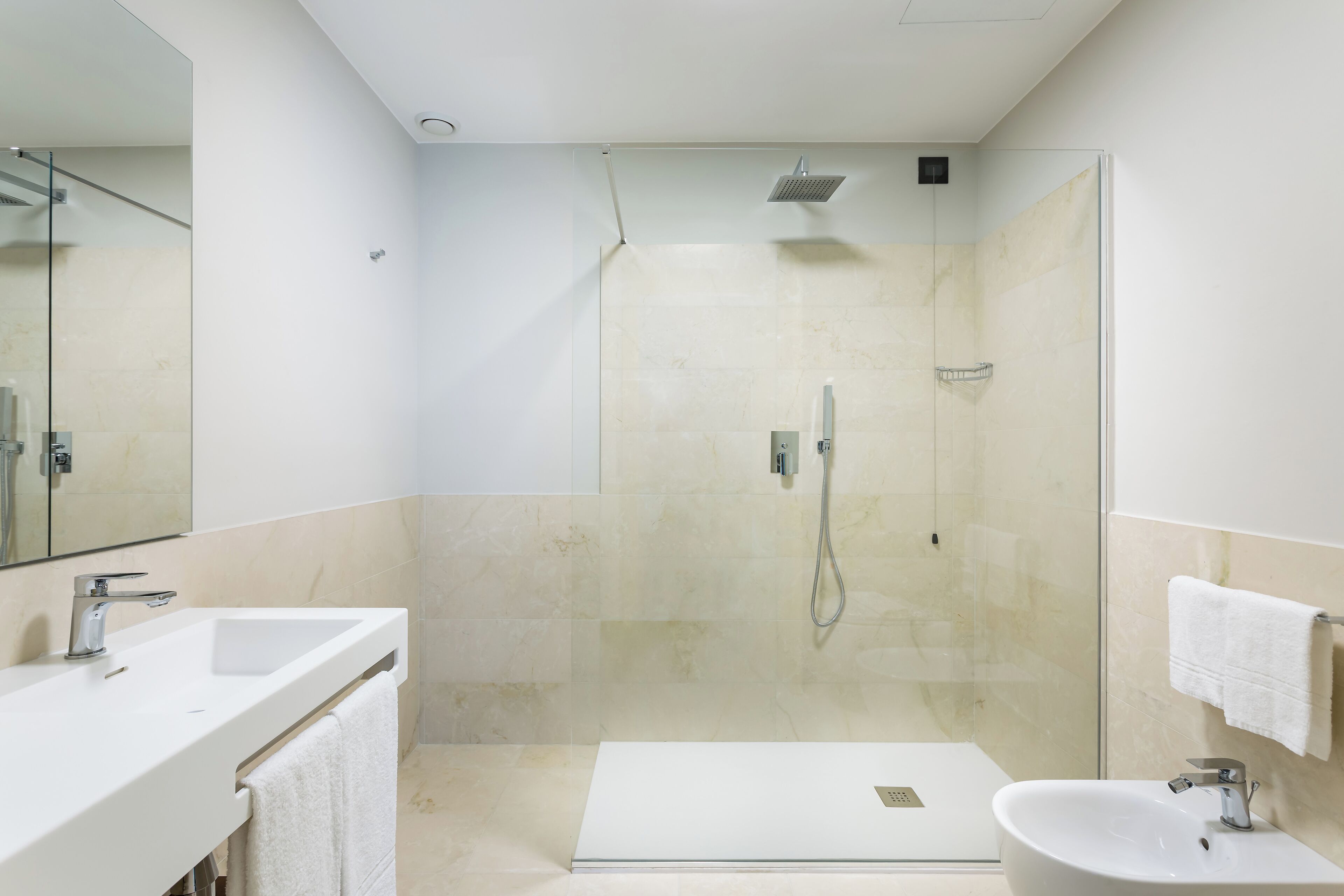A modern bathroom with a glass-enclosed shower, a white sink, and a large mirror.