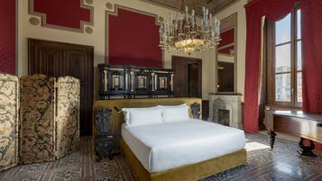 Una cama grande con estructura dorada, un candelabro y una cortina roja.