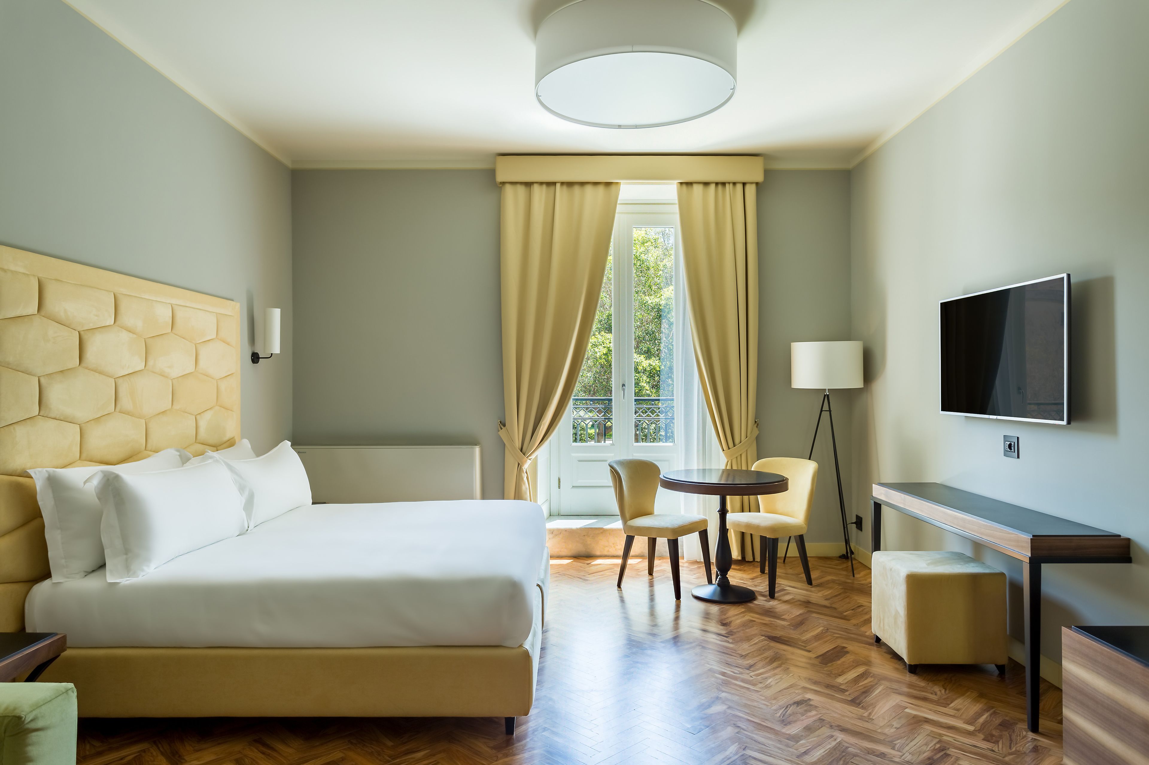 A hotel room with a bed, a desk, a chair, a TV, and a window with curtains.