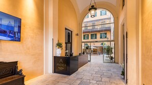 A hotel reception area with a stone floor, a reception desk labeled "Andrea RoomMate Hotel," and a view of the building's exterior through an arched window. - Room of Andrea (Trapani)