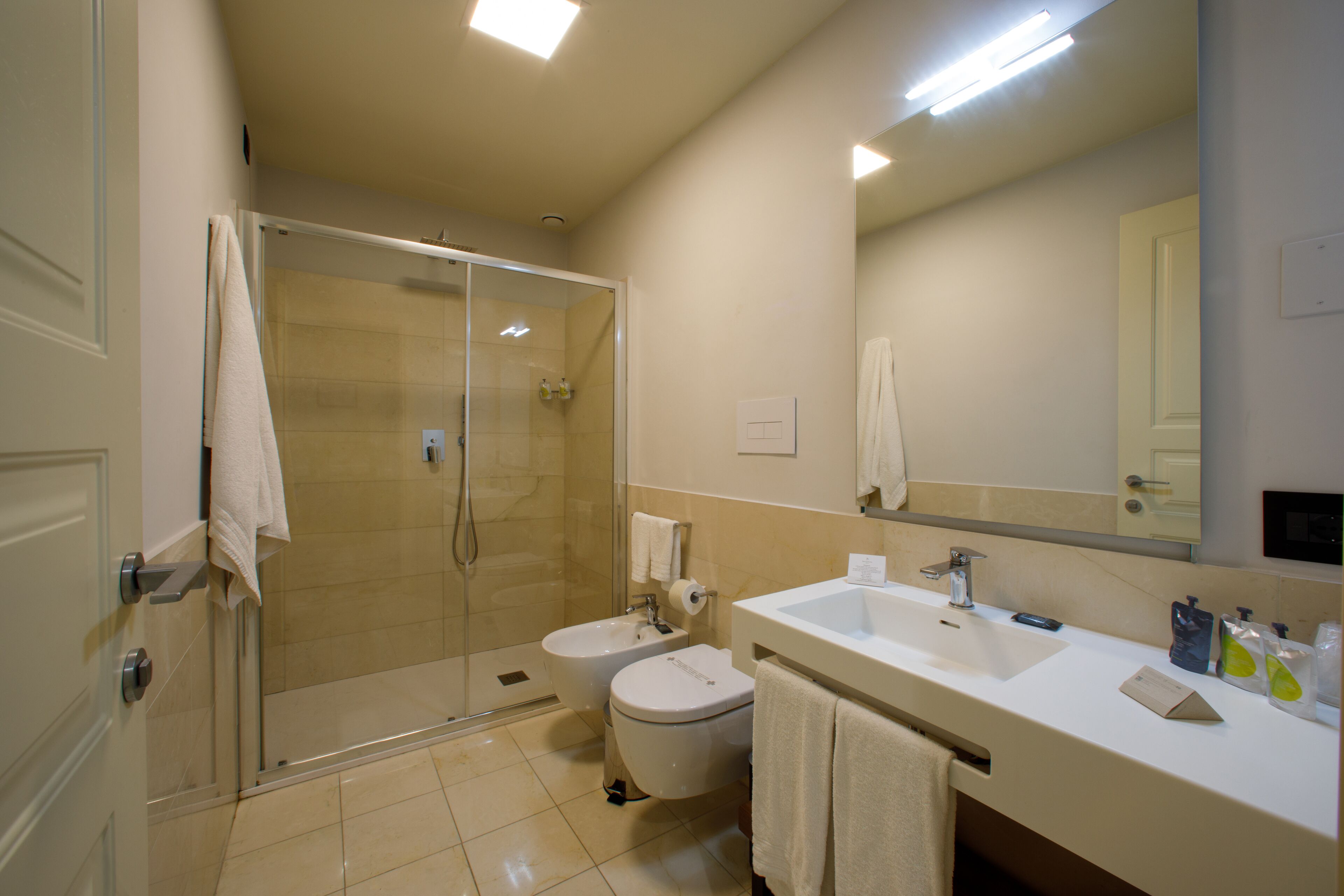 A modern bathroom with a glass-enclosed shower, two sinks, a toilet, and a large mirror.