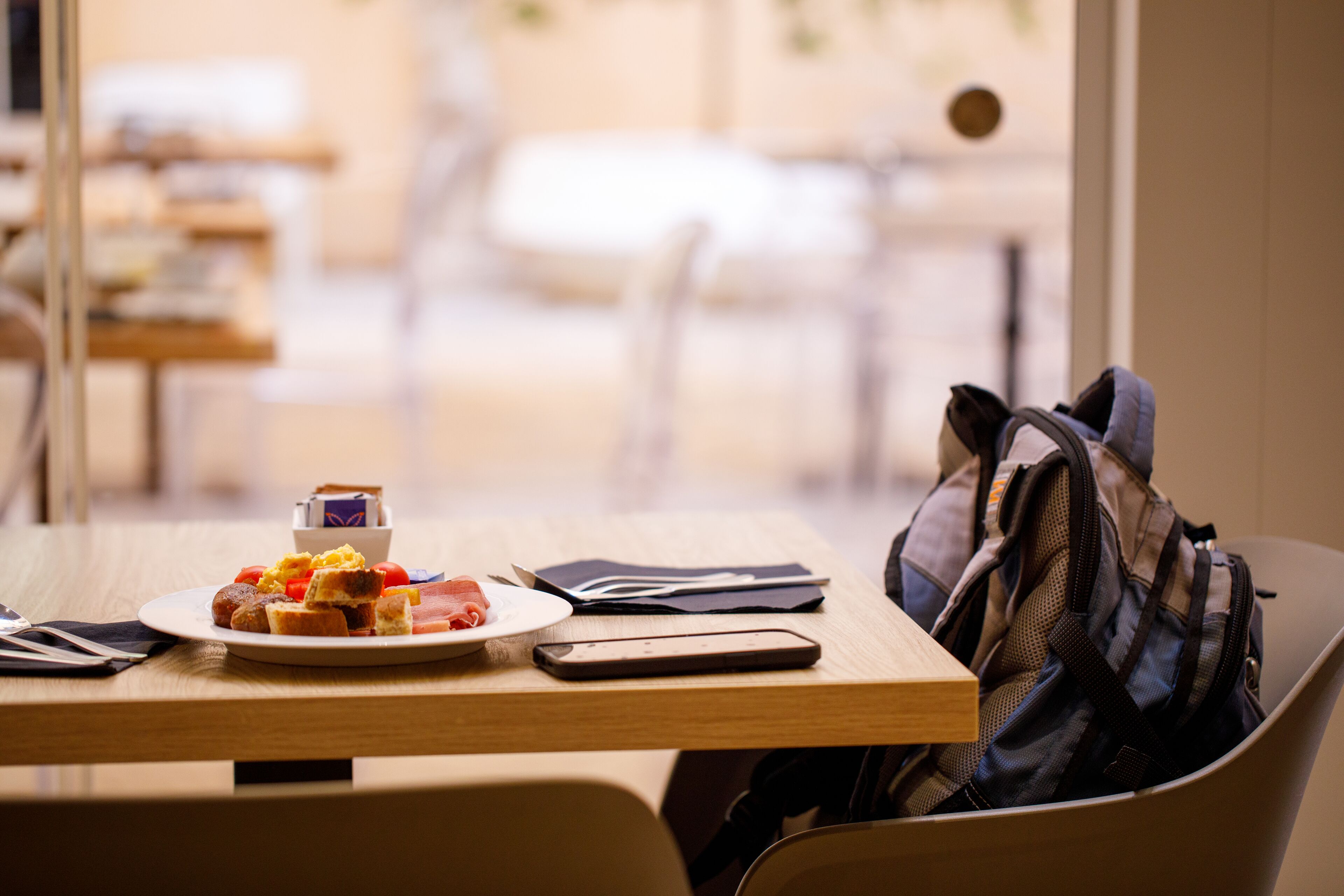 Une table à manger avec une assiette de nourriture, un téléphone intelligent et un sac à dos.
