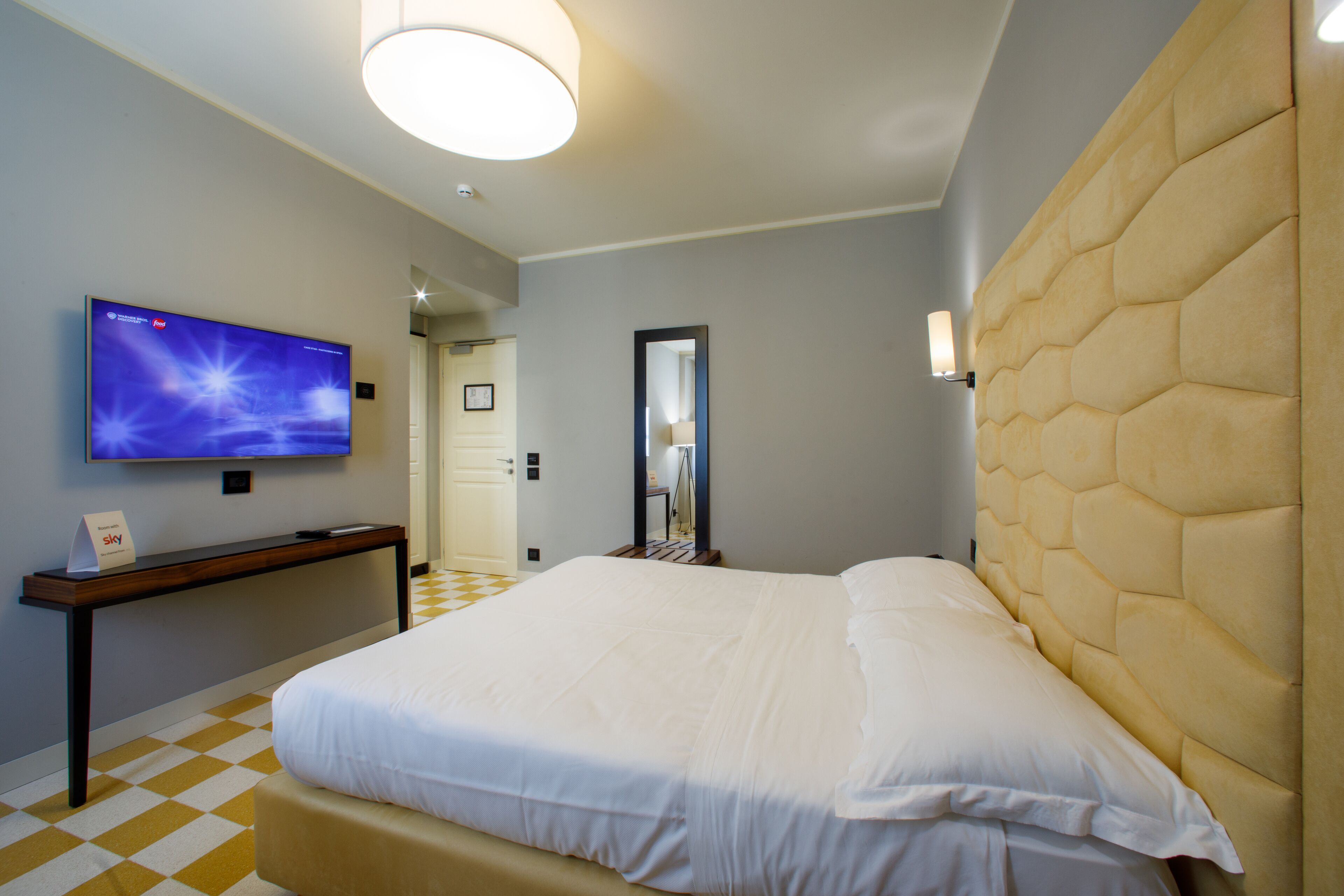 Habitaci ón de hotel con una cama grande, un televisor de pantalla plana en la pared, una mesita de noche y un cartel de recepción.