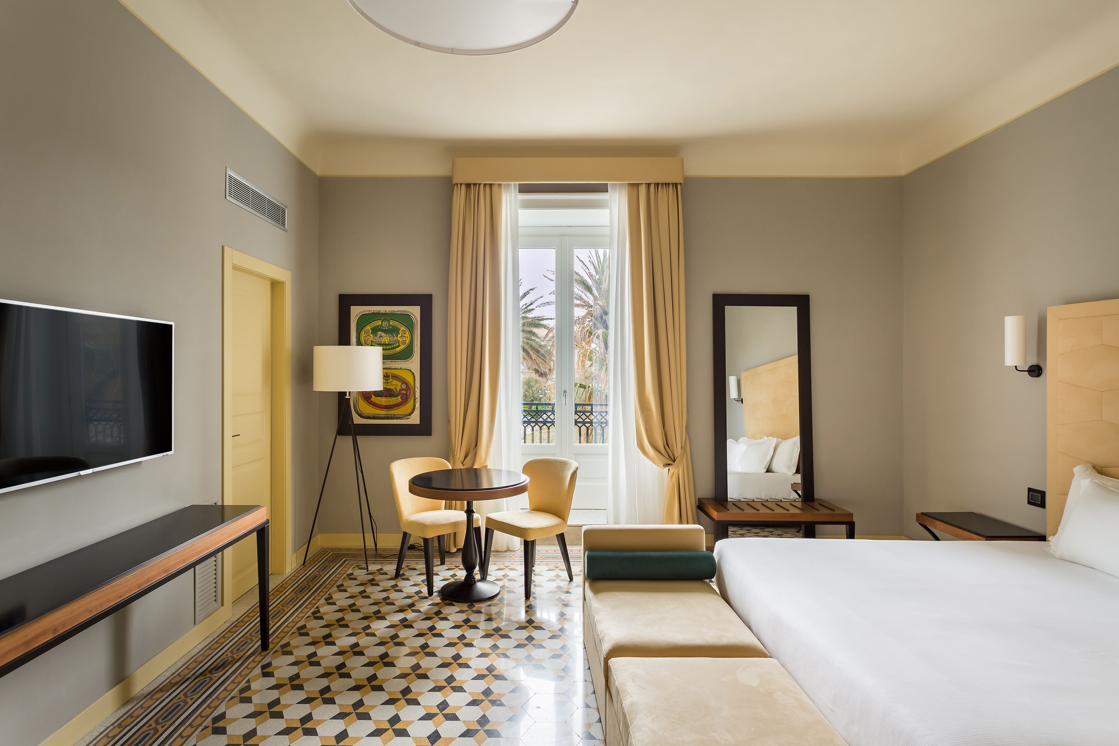 A hotel room with a bed, a desk, a chair, a TV, a lamp, and a window with curtains.