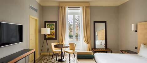 A hotel room with a bed, a desk, a chair, a TV, a lamp, and a window with curtains.