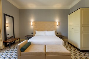 Una camera d'albergo con un letto grande, un comodino, una panca, un armadio e un pavimento decorato.