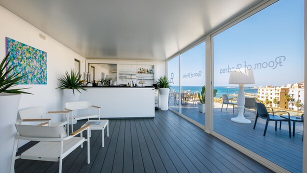 A modern, open-plan living area with a kitchen, seating, and a large balcony with a view of the sea. - Room of Andrea (Trapani)