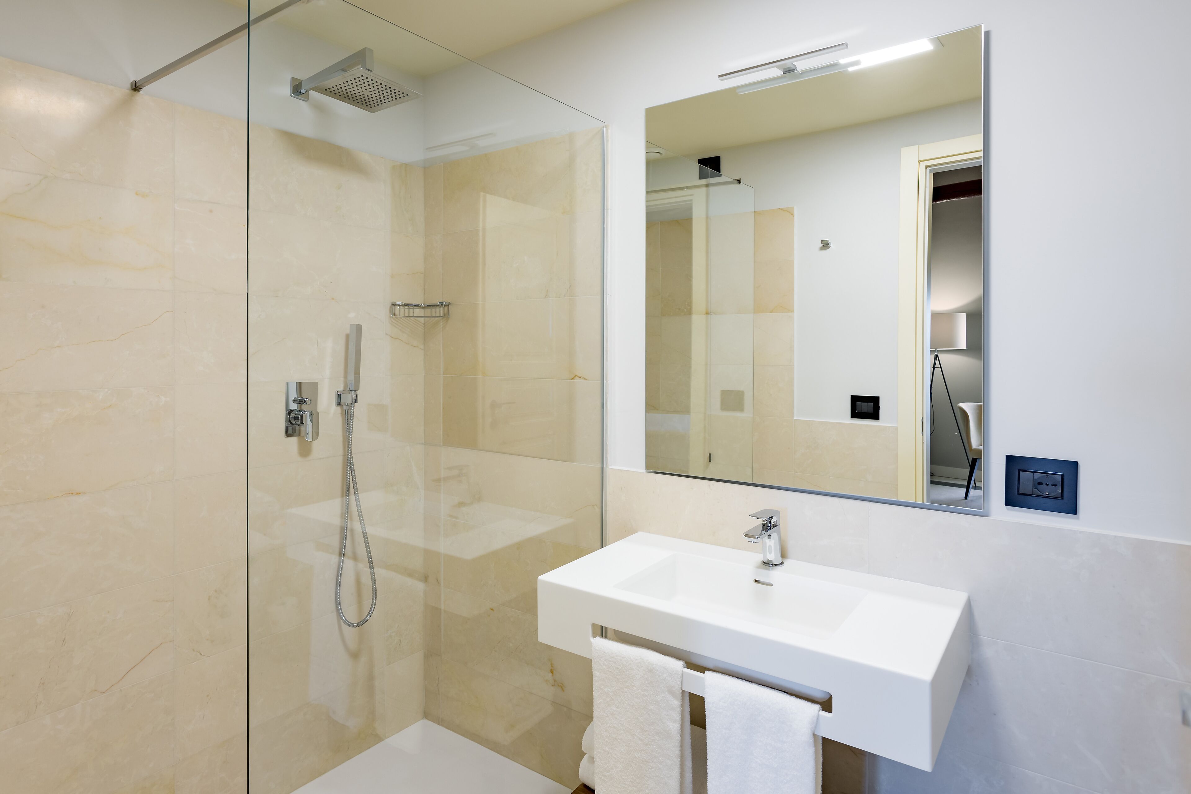 Un baño moderno con ducha envuelta en vidrio, un lavabo blanco y un espejo grande.