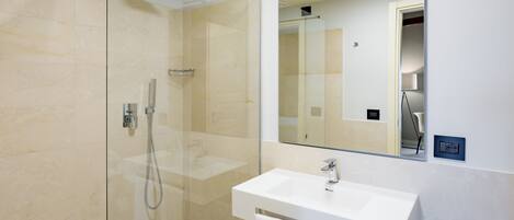 Un baño moderno con ducha envuelta en vidrio, un lavabo blanco y un espejo grande.
