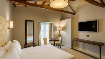 A hotel room with a large bed, a desk, two chairs, a TV, and a lamp.