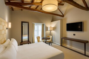A hotel room with a large bed, a desk, two chairs, a TV, and a lamp.