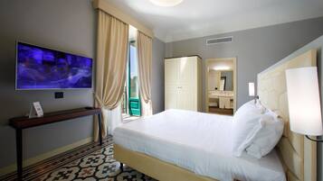 Quarto de hotel com cama, televisão, escrivaninha, guarda-roupa e banheiro visível por uma porta aberta.