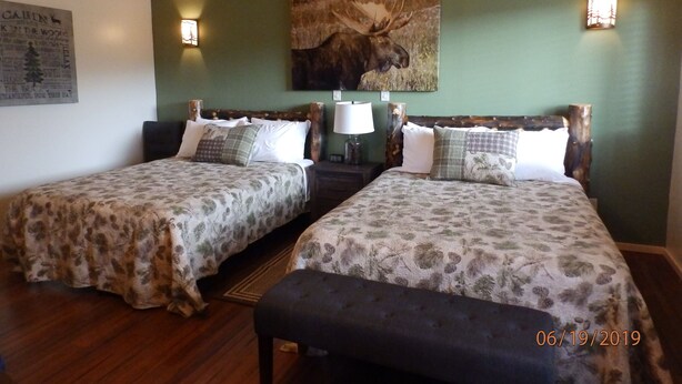 A room with two beds, each with floral-patterned bedding, wooden headboards, and a mounted moose picture on the wall. -  Denali Wildlife Moose Cabin  Luxury with a touch of Rustic (Healy)
