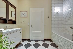 A bathroom with a white sink, a mirror, a door, and a white bathtub.