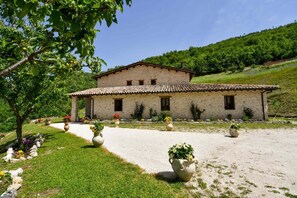A stone building with a tiled roof, surrounded by a gravel driveway and flower beds. - Agriturismo La Valle Dei Bronzetti (Cascia)