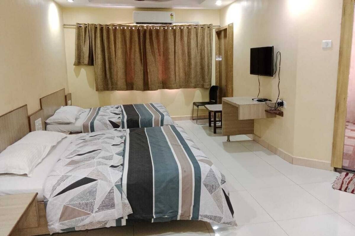 Un dormitorio con dos camas, un escritorio, una silla, un televisor y un equipo de aire acondicionado.