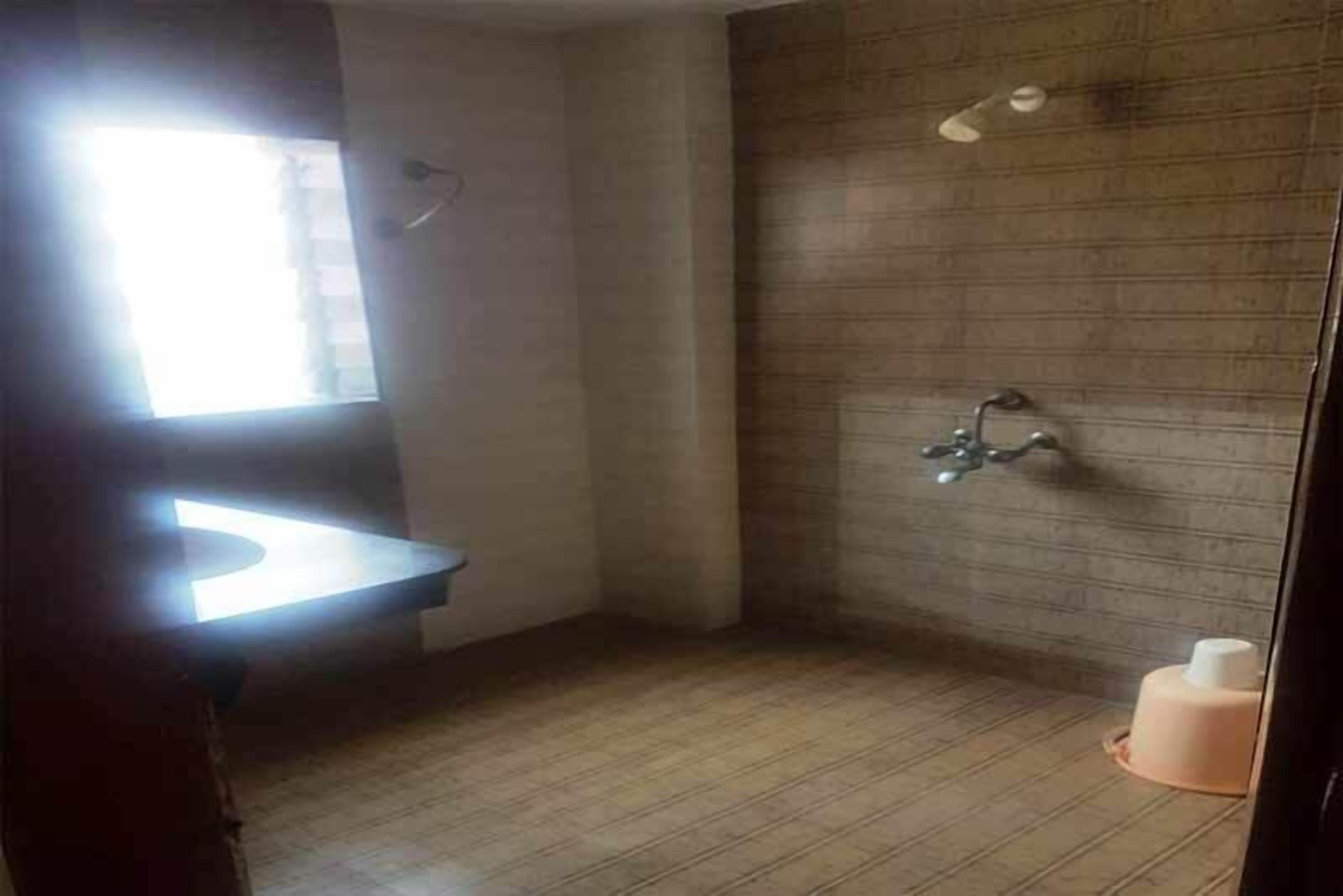 Un baño con suelo de madera, un lavabo, una ducha con grifo empotrado en la pared y una ventana que proporciona luz natural.