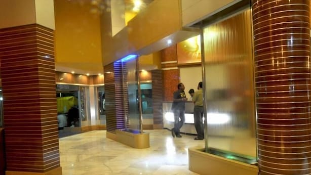 A hotel lobby with a marble floor, glass partitions, and wooden accents. - Hotel Sharan (Rahata)