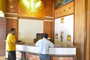 Uma área de recepção de hotel com um balcão de mármore, um relógio de parede grande e um quadro pendurado na parede.