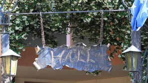 Un letrero con la palabra 'HALL' sobre una puerta, rodeado de faroles decorativos y follaje.